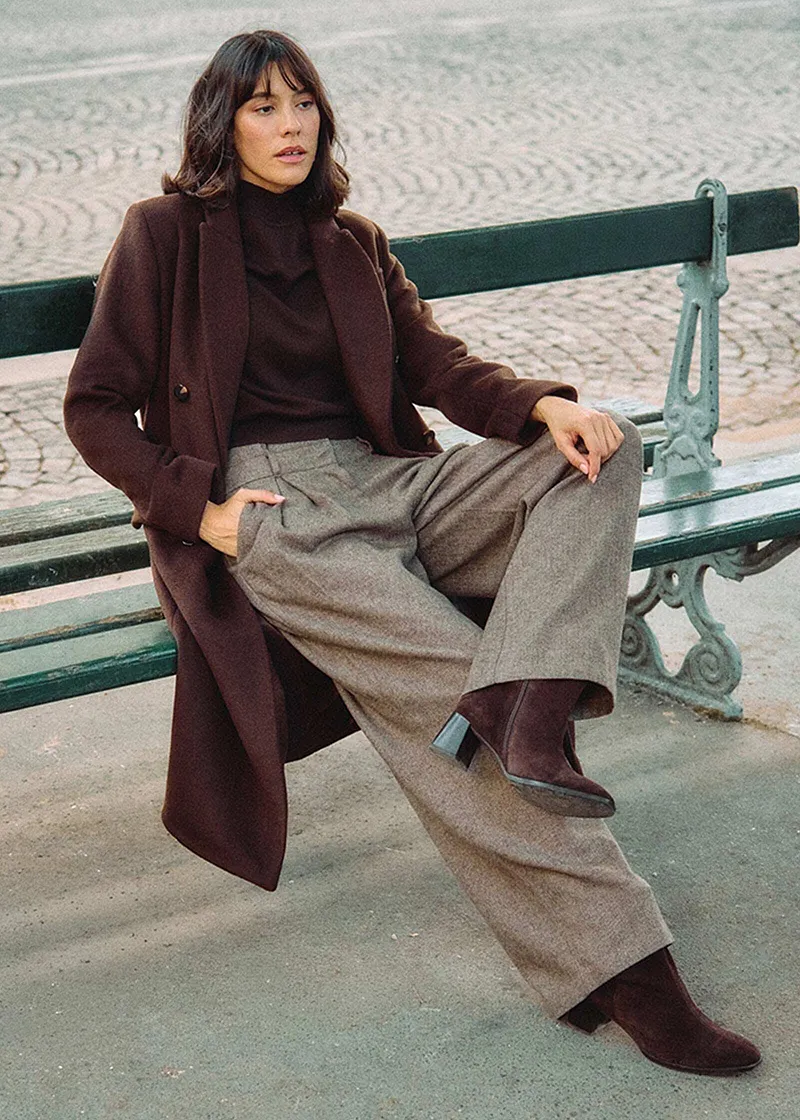 Lång brun kappa, polotröja och vid tweedbyxa.