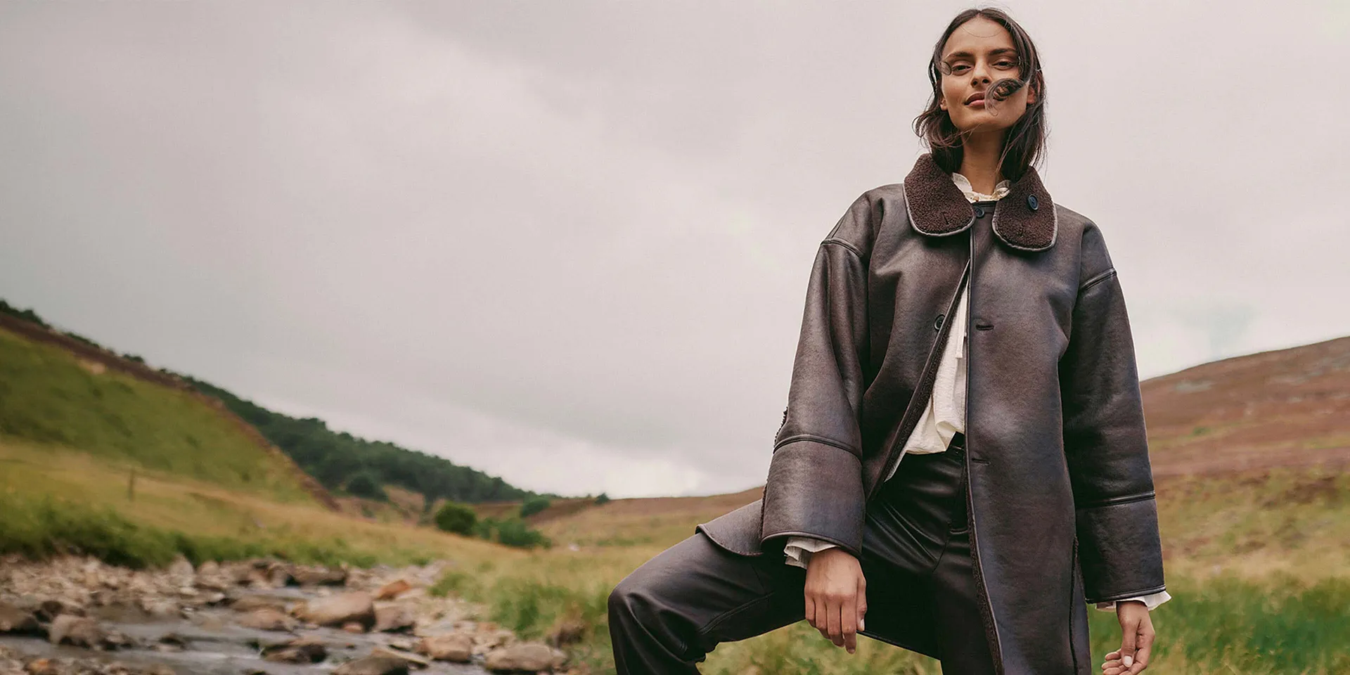 Elegant, brun kappa i skinn med stor krage kombinerad med en ljus topp och mörka byxor.