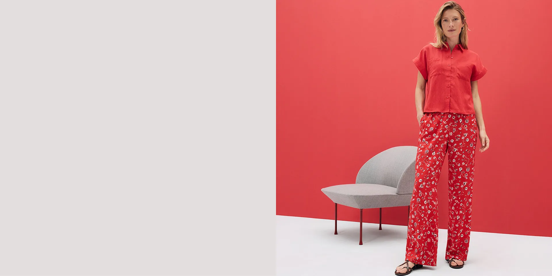 Röd kortärmad skjorta och vida byxor med blommigt mönster. Somrig outfit mot en ljusröd bakgrund.