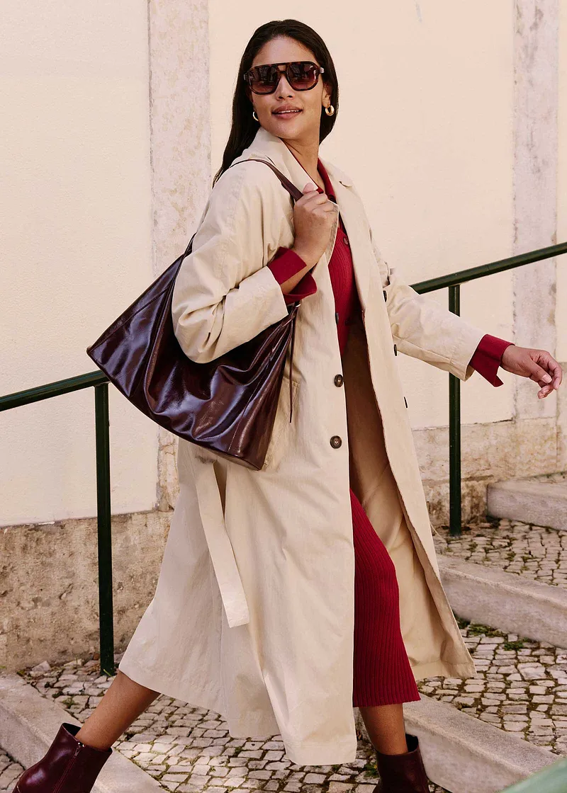 Elegant beige trenchcoat över röd klänning, bruna stövlar och stor väska.

