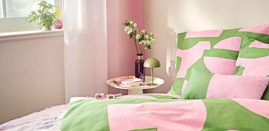 Fräscha sängkläder i rosa och grönt ger en somrig stämning i det ljusa sovrummet.