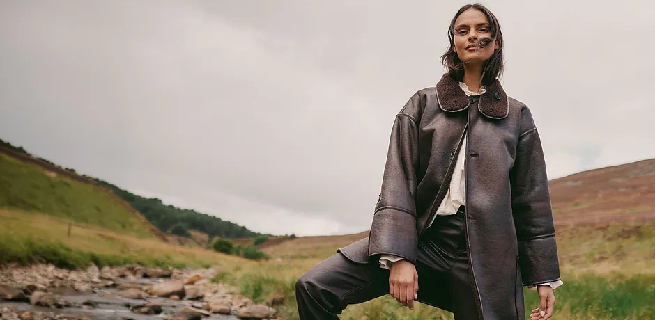 Elegant, brun kappa i skinn med stor krage kombinerad med en ljus topp och mörka byxor.