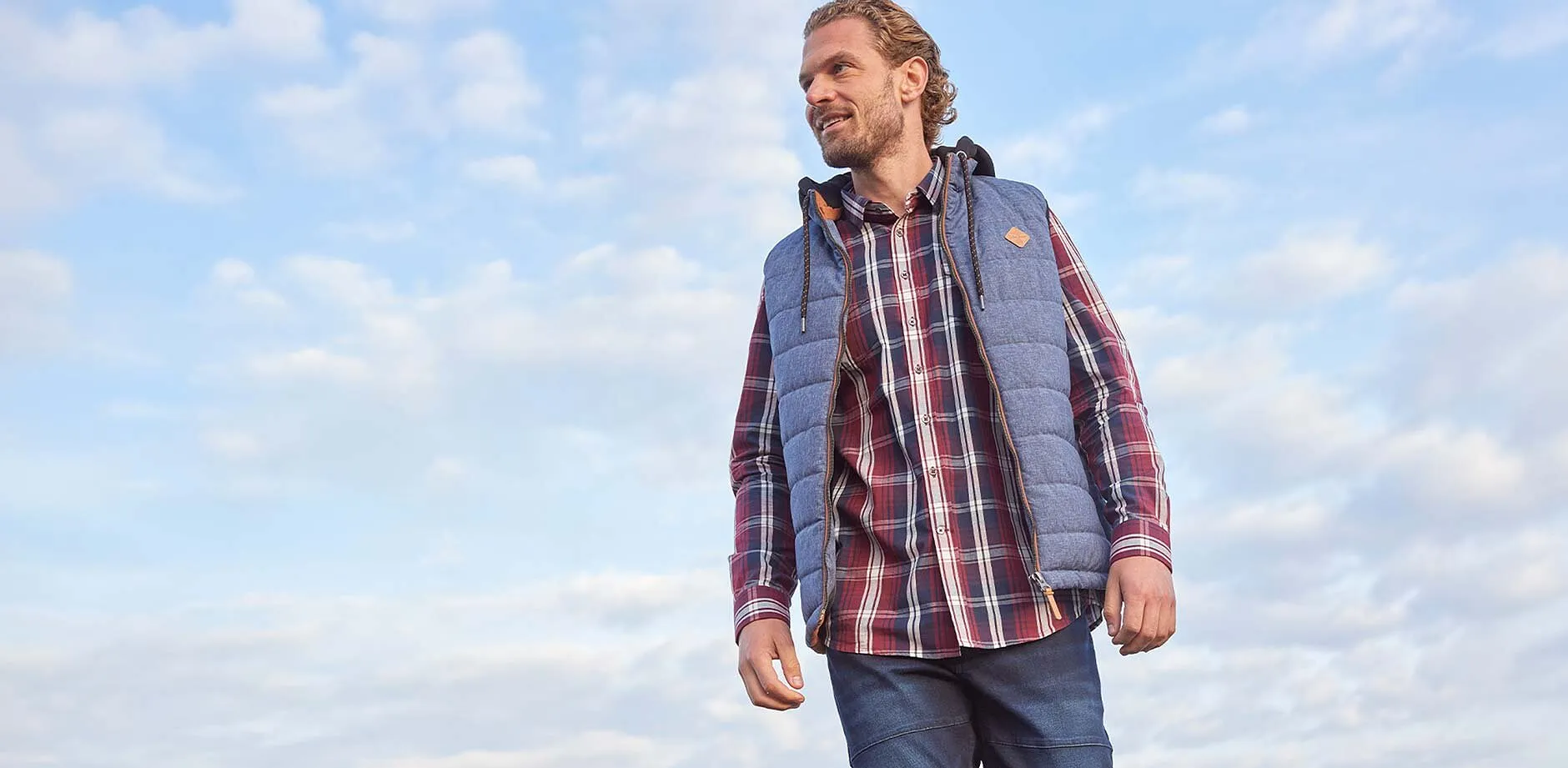 Rutig skjorta, bl&aring; jeans och en v&auml;st.
