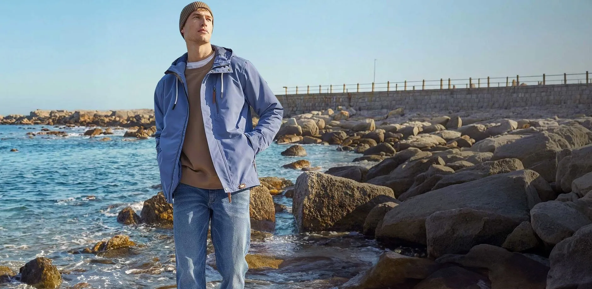 Stilig bl&aring; funktionsjacka och ljusa jeans p&aring; stranden.

