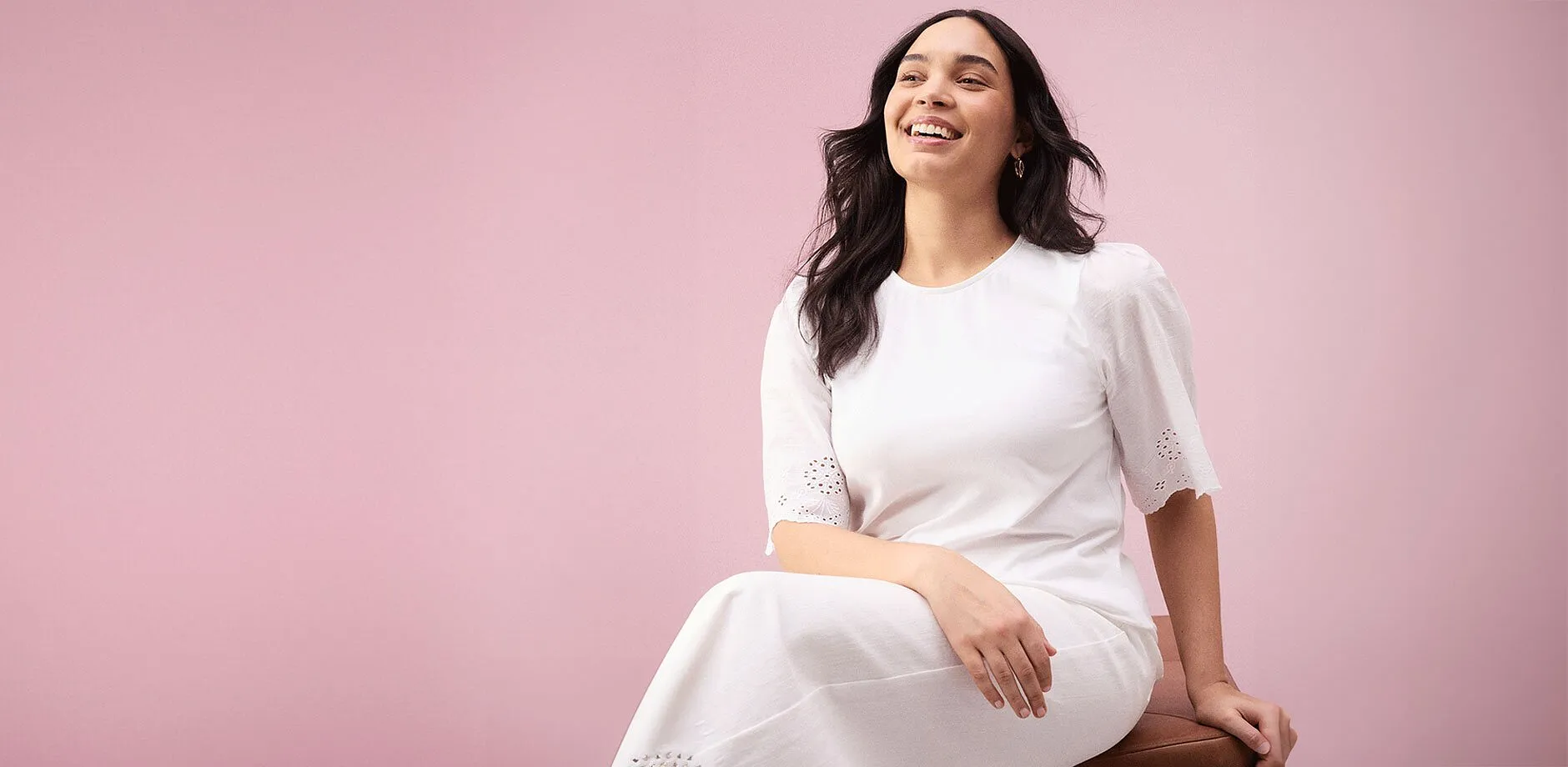 En str&aring;lande kvinna i en enkel vit kl&auml;nning med korta &auml;rmar och h&aring;lbroderi.

