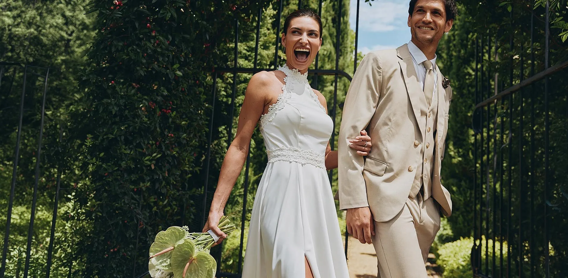 Elegant brudpar i solsken: hon i vit kl&auml;nning, han i beige kostym