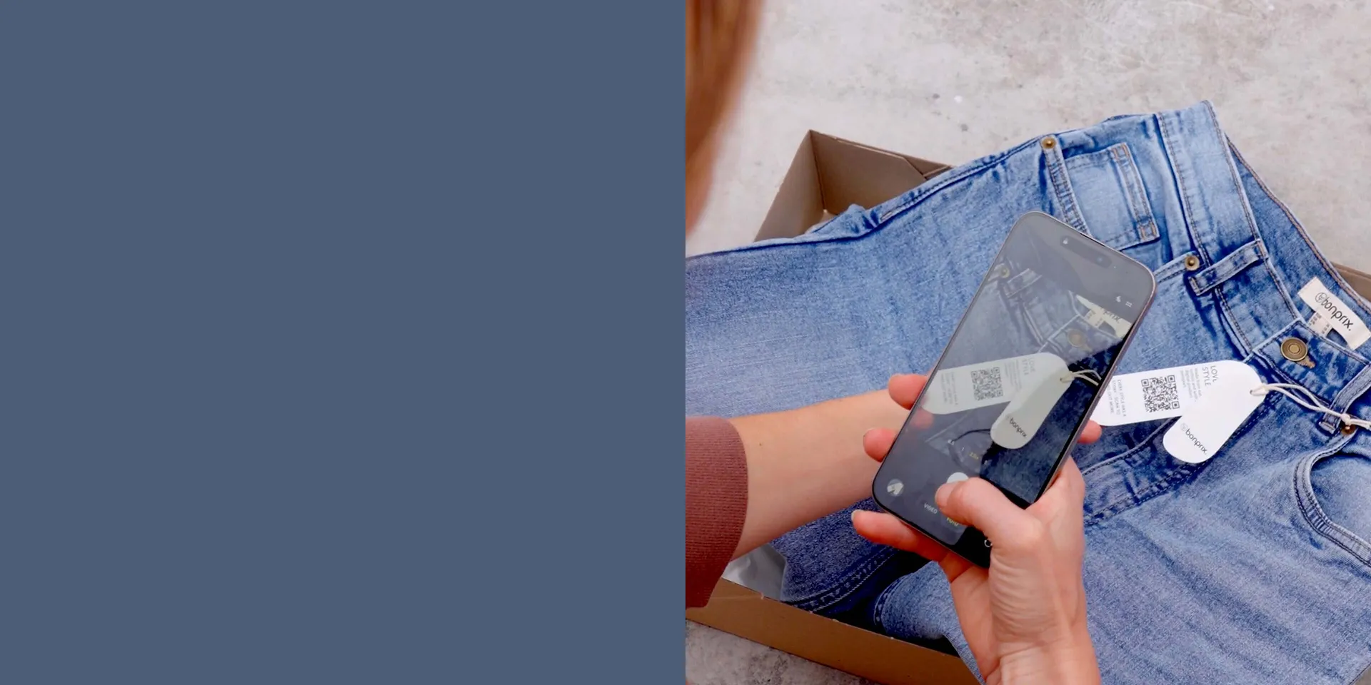 Bl&aring; jeans p&aring; gr&aring; bakgrund. H&auml;nder h&aring;ller en smartphone &ouml;ver kl&auml;derna.