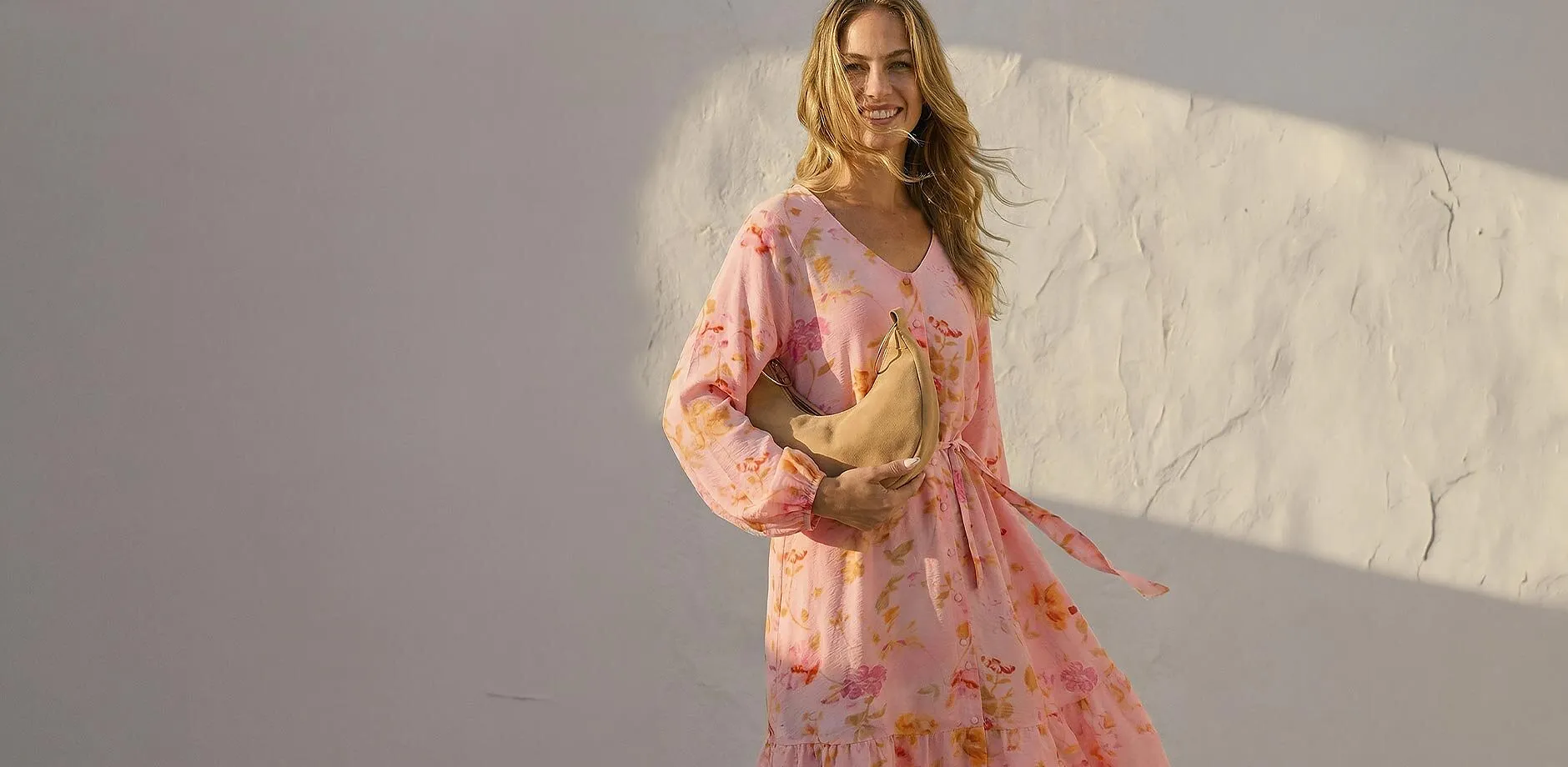 Frau tr&auml;gt luftiges gebl&uuml;mtes rosa Sommerkleid mit langen &Auml;rmeln.