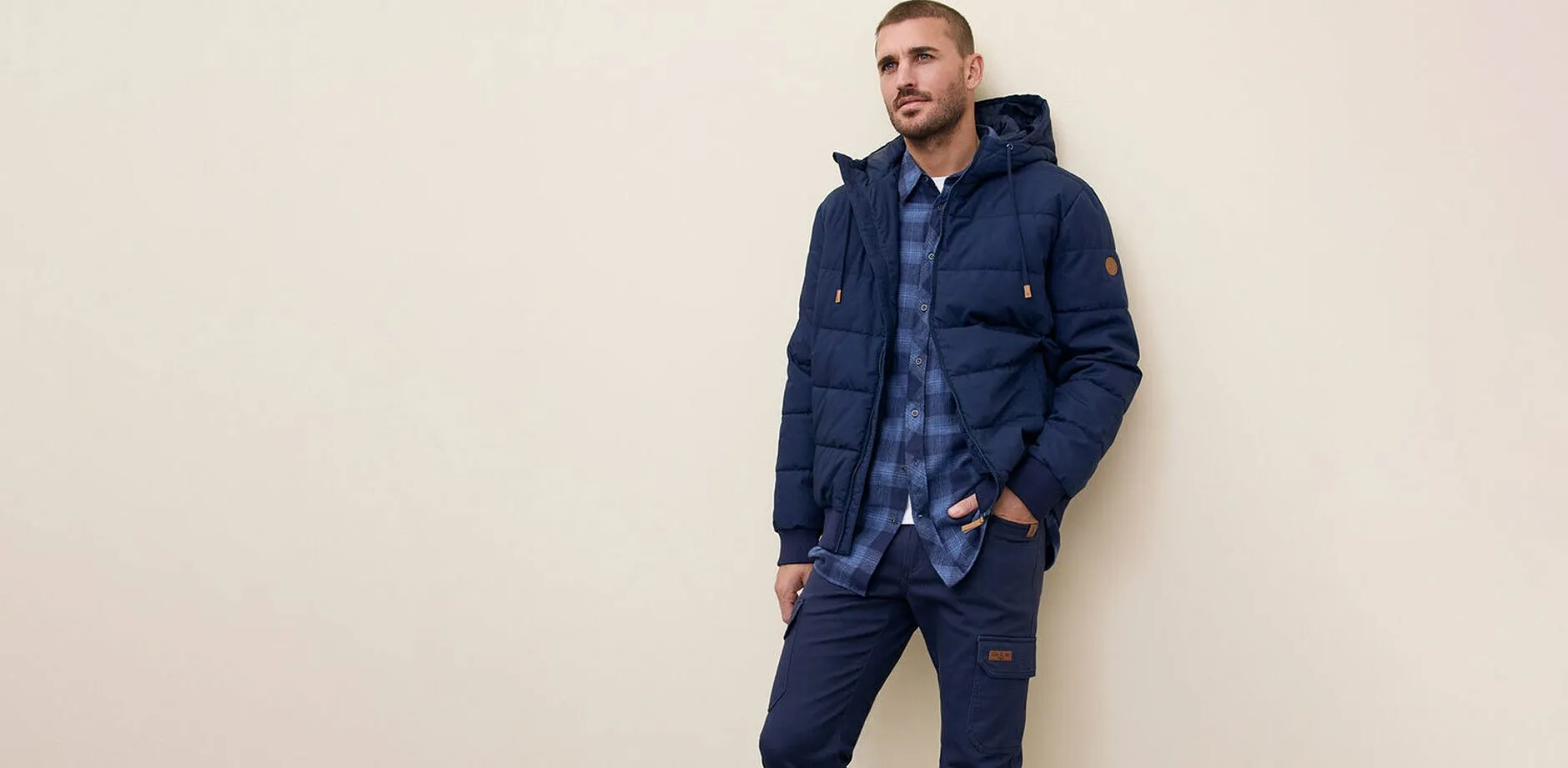 Marinbl&aring; t&auml;ckjacka, jeans och bl&aring;rutig skjorta.

