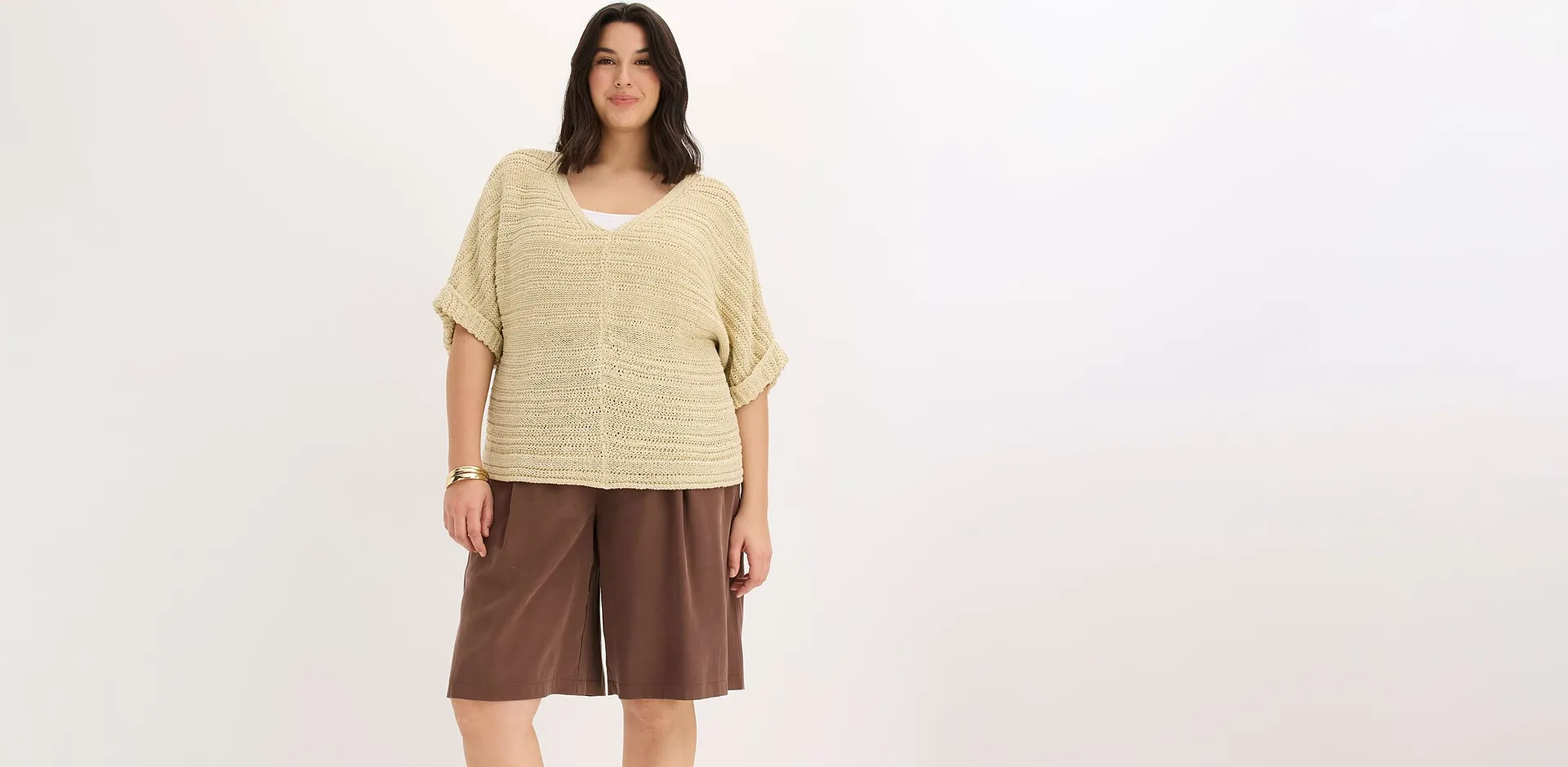 Kvinna b&auml;r beige stickad topp och bruna vida shorts.

