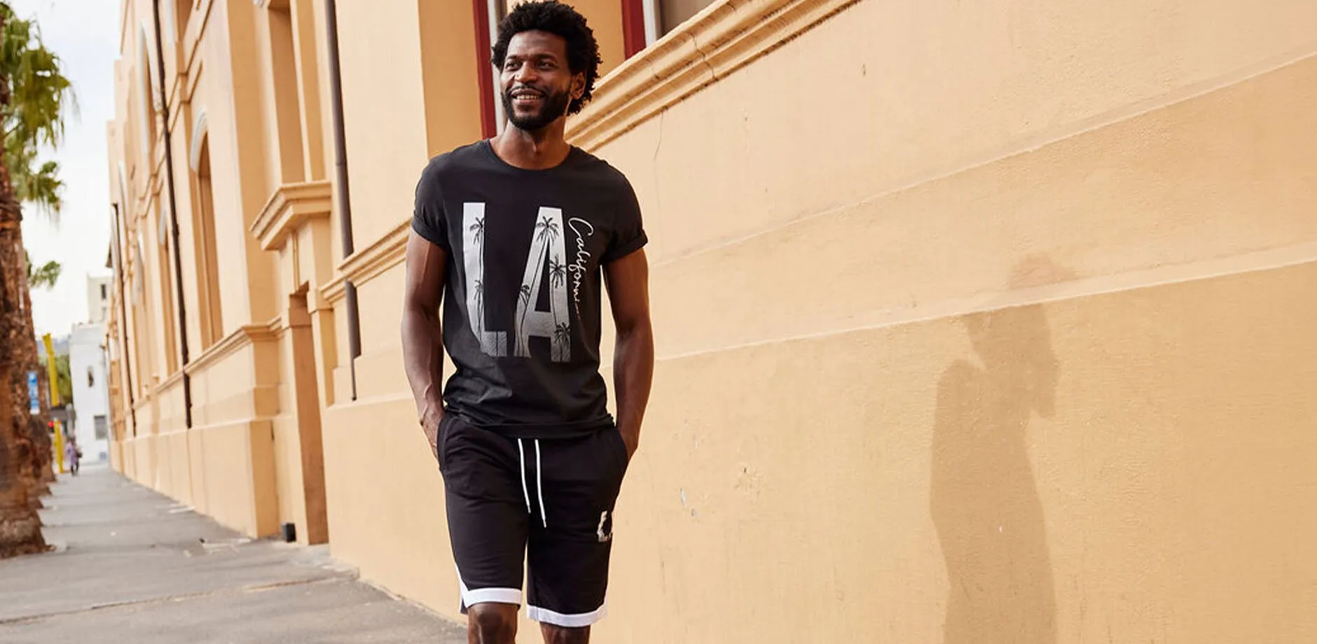 Avslappnat kl&auml;dd i en svart T-shirt med "LA"-tryck och matchande joggingbyxor.

