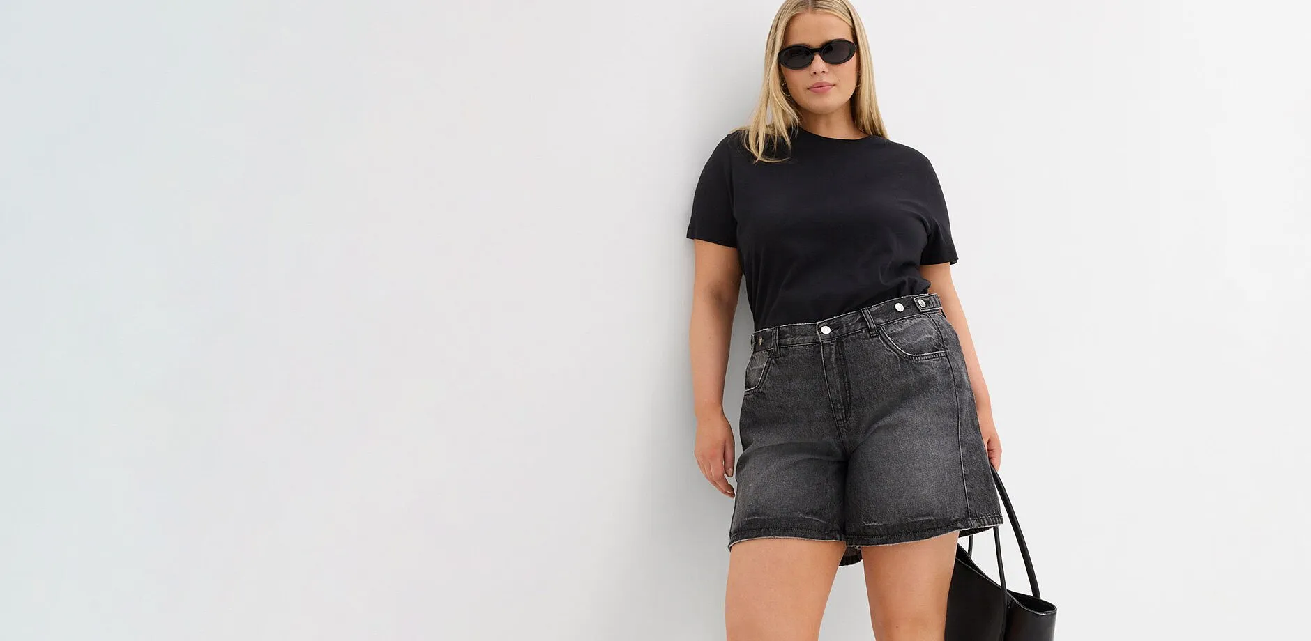 Svart t-shirt, vida gr&aring; jeansshorts, solglas&ouml;gon och en svart v&auml;ska.

