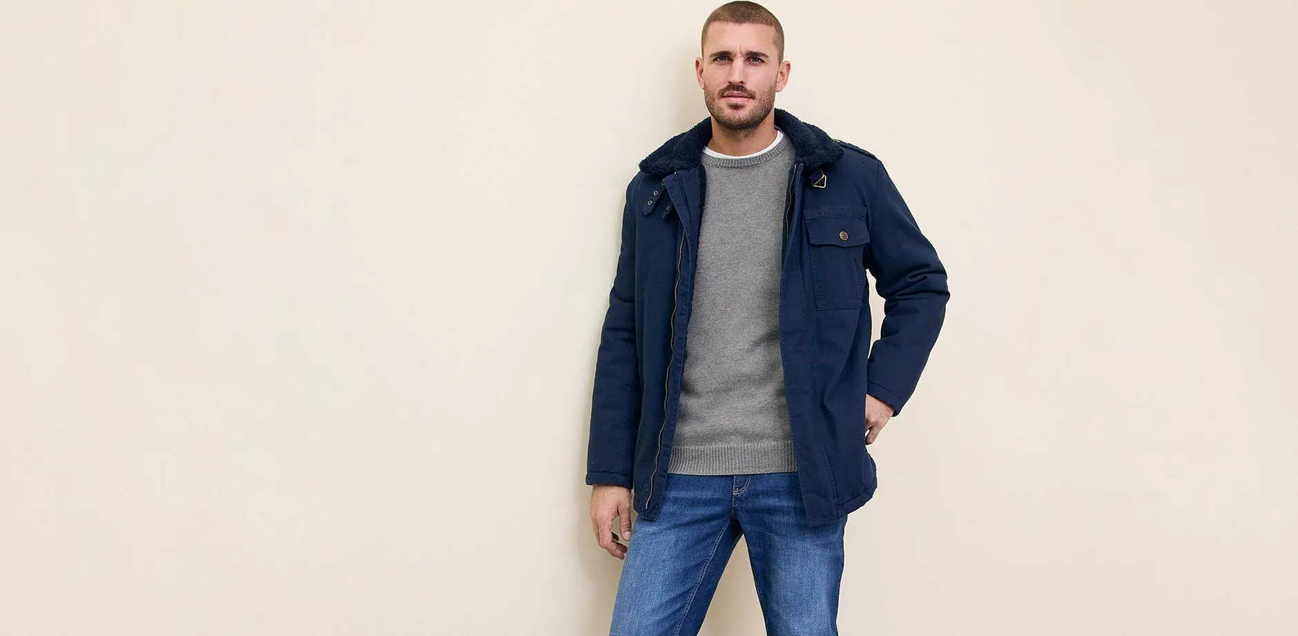 En m&ouml;rkbl&aring; jacka &ouml;ver en gr&aring; tr&ouml;ja, kombinerat med bl&aring; jeans.

