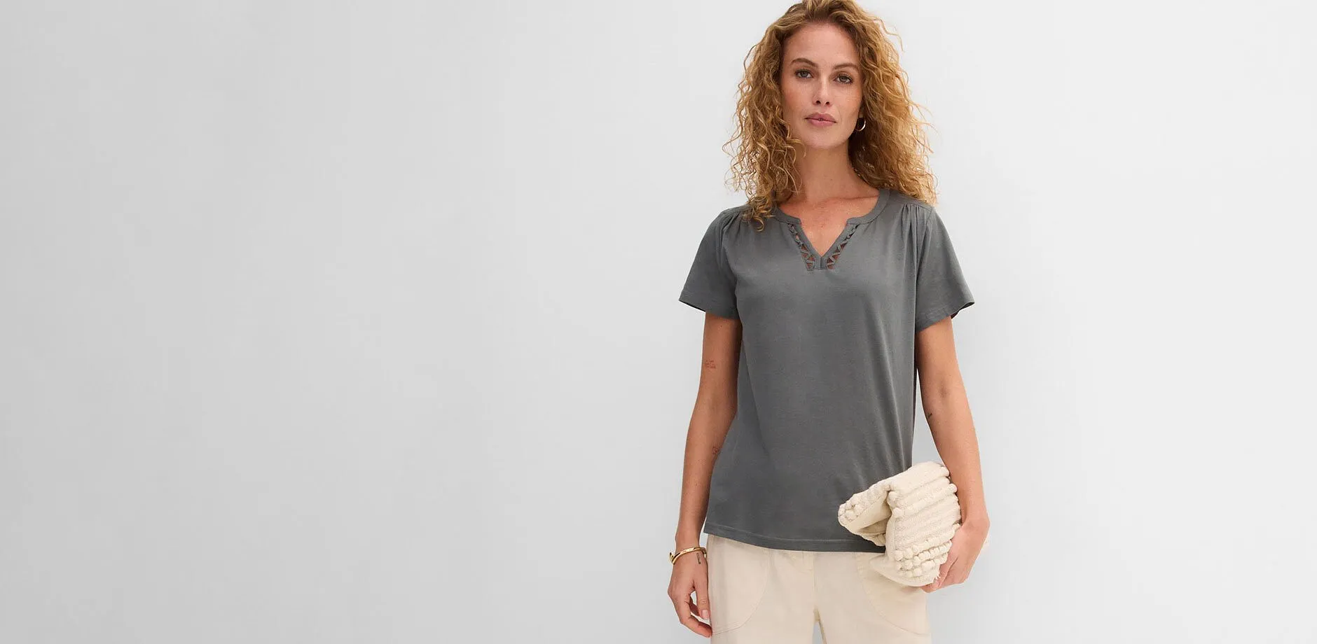 Gr&aring; T-shirt med V-ringning, ljusa byxor och beige kuvertv&auml;ska med strukturm&ouml;nster.