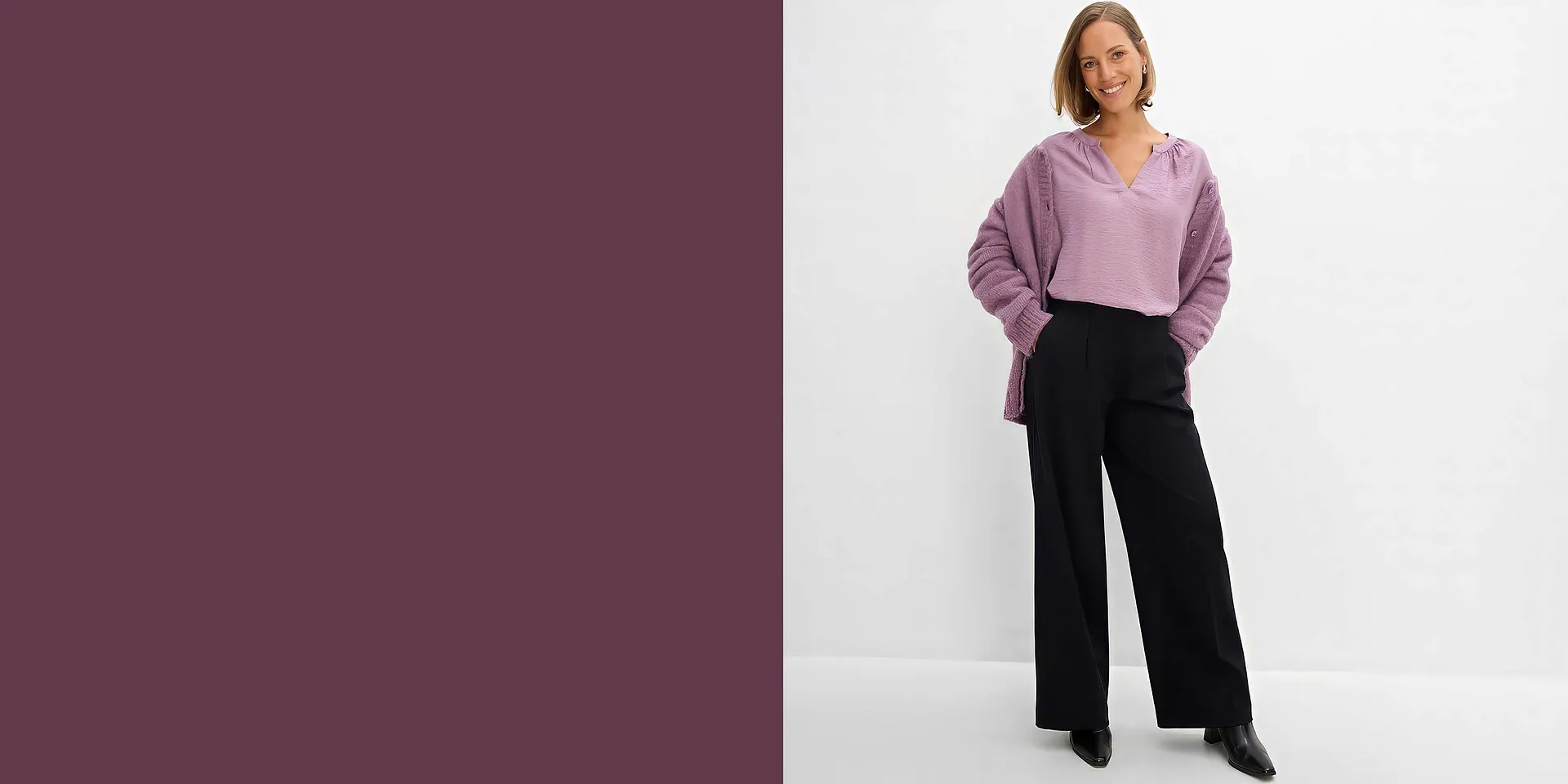 Hon b&auml;r en lila blus, en cardigan och en svart, vid byxa.