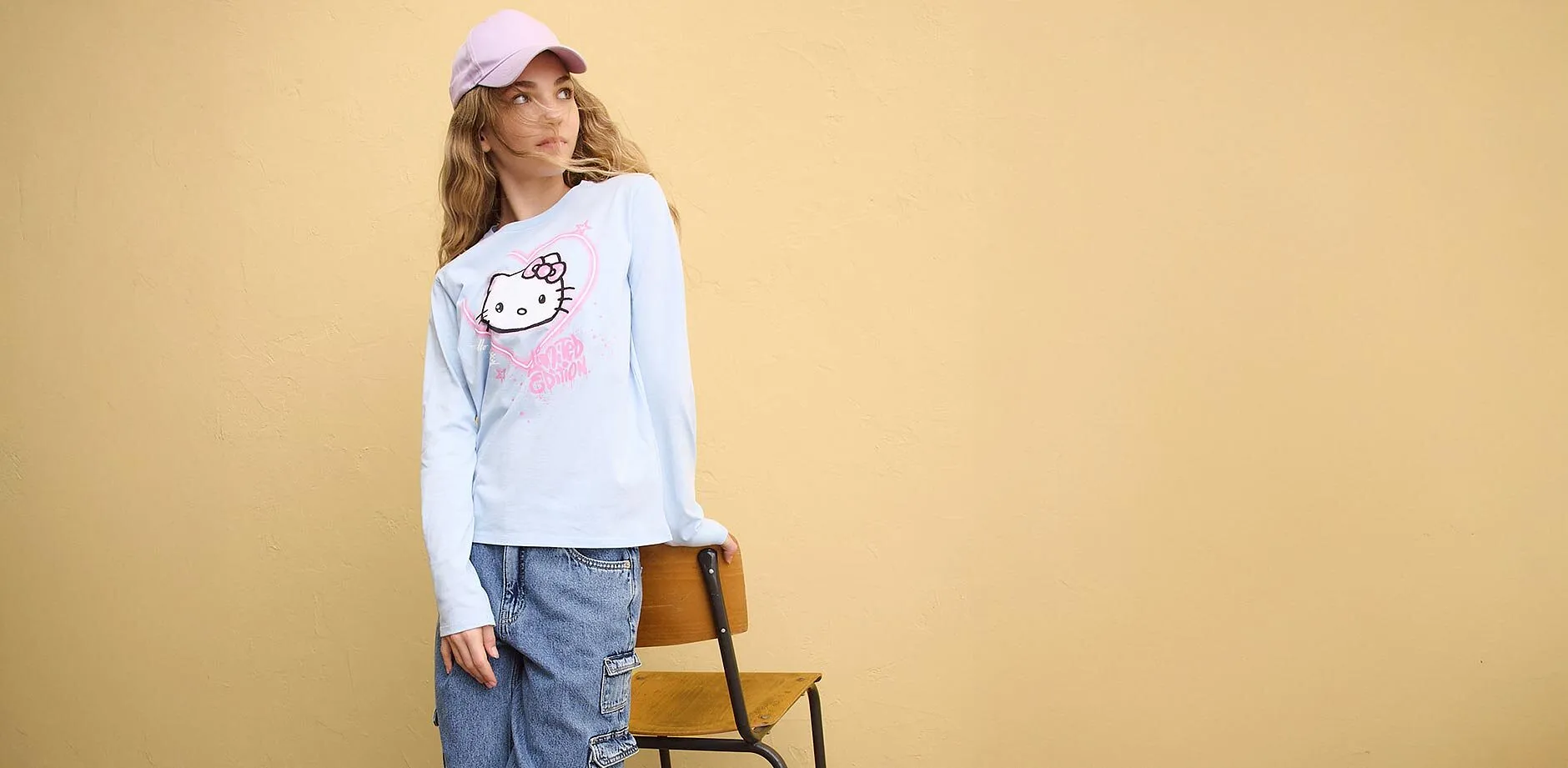 Bl&aring; l&aring;ng&auml;rmad tr&ouml;ja med Hello Kitty-tryck, bl&aring; jeans och rosa keps.