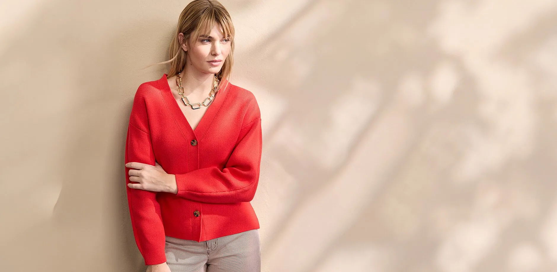 En r&ouml;d stickad kofta med V-ringning och knappar, kombinerad med en i&ouml;gonfallande guldkedja.