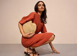 Rostfärgad jumpsuit med korta ärmar, kompletterad med en handväska i strålook och fina sandaler.