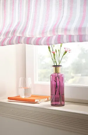 Randiga gardiner i pastellfärger pryder fönstret. Nedanför finns en rosa vas med blommor.