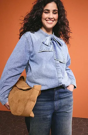 Ljusblå jeansblus med rosettkrage, mörka jeans och en brun läderväska för en avslappnad vardagslook.