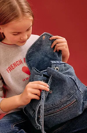 Grå sweatshirt med röd text och blå denimryggsäck. Ledig vardagslook för barn.