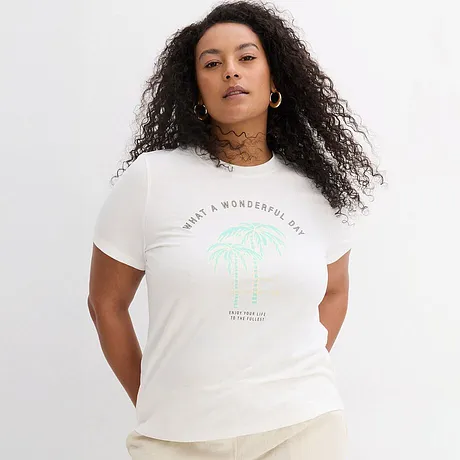 Vit T-shirt med grönt palmtryck och bokstäver, kombinerad med ljusa byxor.