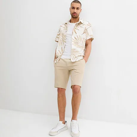 Somrig outfit med beige shorts och en vit skjorta med palmmönster.