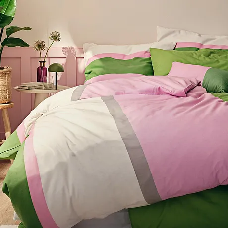 Fräscha sängkläder i rosa, vitt och grönt pryder den mysiga sängen i sovrummet.