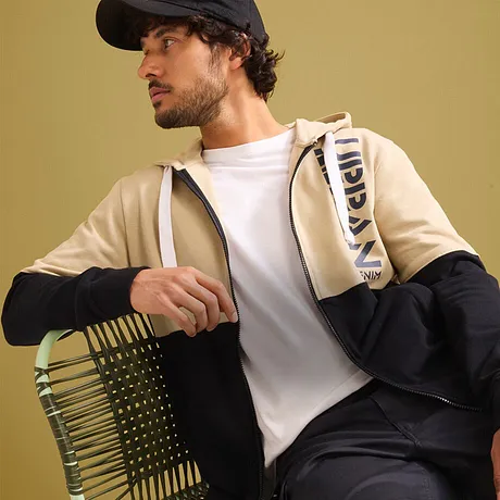 Urban look: beige jacka, vit T-shirt, mörka byxor och keps.
