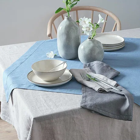 Blå och grå dukar pryder ett bord och kompletteras av stilrena vita blomvaser.
 
