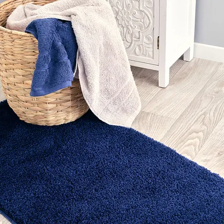 Mjuka handdukar i blått och beige som ligger i en korg på en fluffig matta.