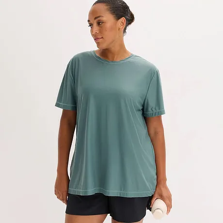 En ledig, salviagrön funktionströja med rund halsringning och korta ärmar kombinerad med mörka shorts.