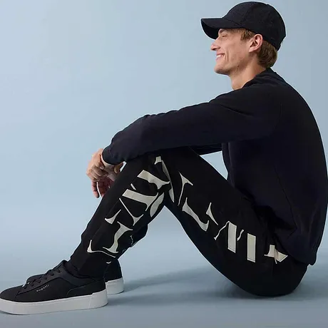 Sweatbyxor, mörk tröja och sneakers kompletterar den sportiga looken.