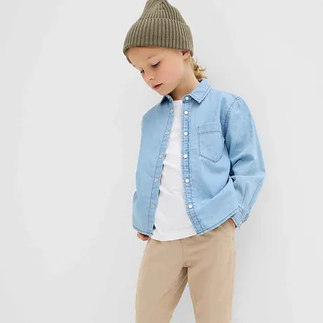 Ljusblå jeansskjorta över vit T-shirt, beige byxor och grön stickad mössa: avslappnad barnlook.