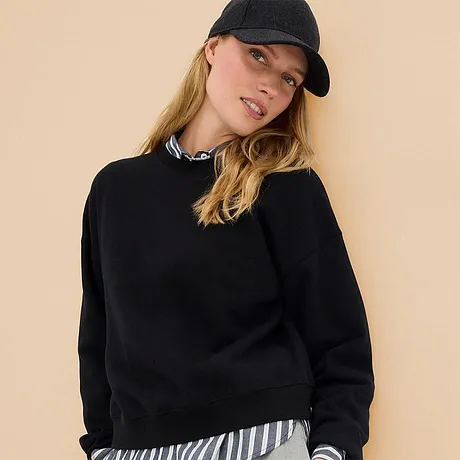 Svart sweatshirt kombinerat med en randig skjorta och en avslappnad keps.