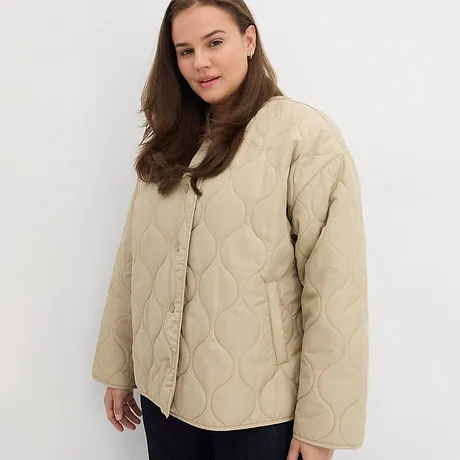Beige täckjacka med knappar kombinerad med ett par mörka byxor.