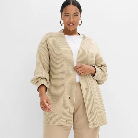 Beige, grovstickad oversizecardigan kombinerad med ett vitt linne och en ljusbeige byxa.