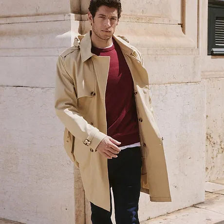 Elegant beige trenchcoat över en röd tröja och mörka jeans.