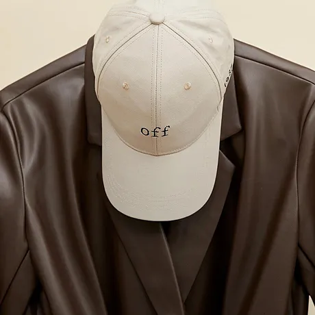 En beige keps och en brun läderjacka hänger prydligt på en galge.

