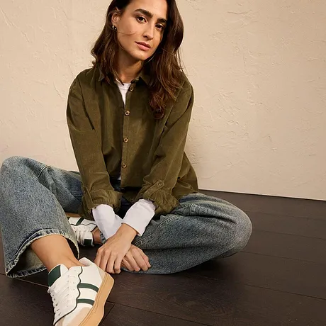 Olivgrön jacka med jeans och vita sneakers med gröna ränder.

