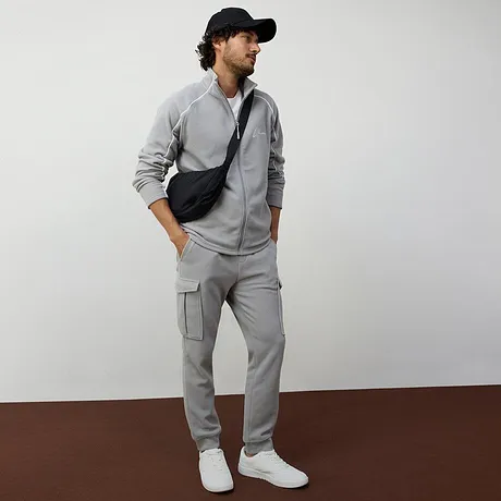 Ledig grå träningsoverall med jacka med dragkedja och vita sneakers.