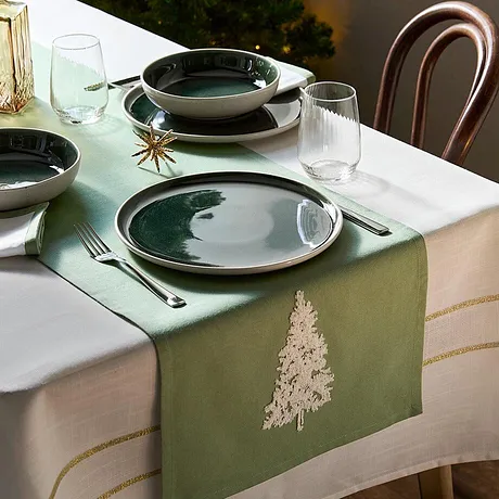 En grön bordslöpare med granbroderi pryder ett festligt dukat julbord.