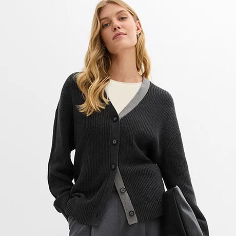 Mörk cardigan över vit topp kombinerad med grå kjol och svart handväska.