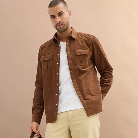 Brun skjorta över vit t-shirt, kombinerat med ljusa byxor.

