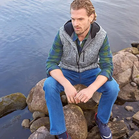 En mönstrad väst över en grön skjorta, kombinerat med blå jeans.

