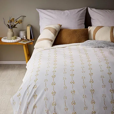 Vita sängkläder, beige-guldmönster och flera dekorativa kuddar.

