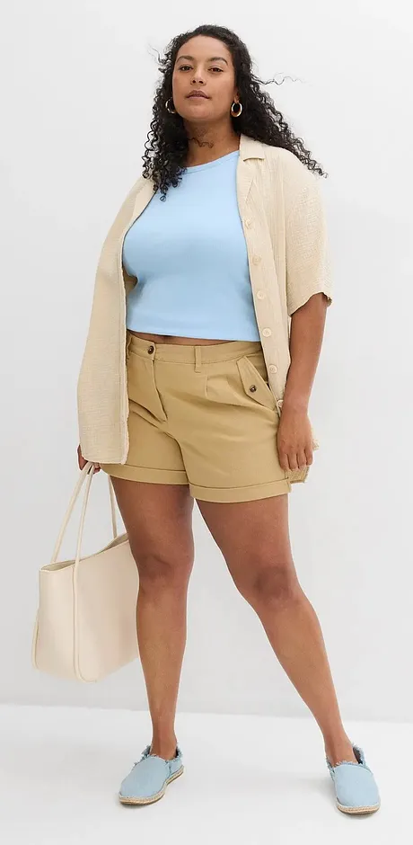 Somrig outfit med ljusblå topp, beige cardigan, khakifärgade shorts och matchande skor.
