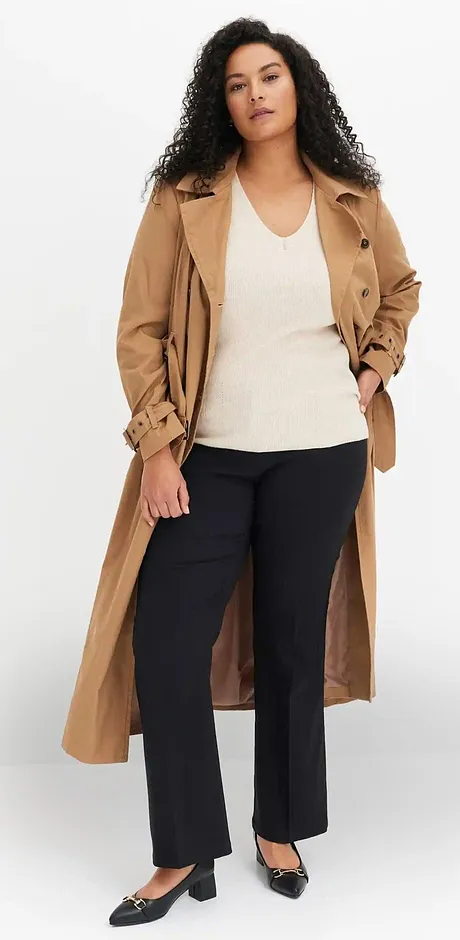 Klassisk beige trenchcoat över ett vitt linne och mörka byxor.