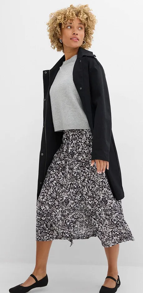 Elegant svart kappa, grå överdel och lång, mönstrad kjol kombinerade med lågskor.