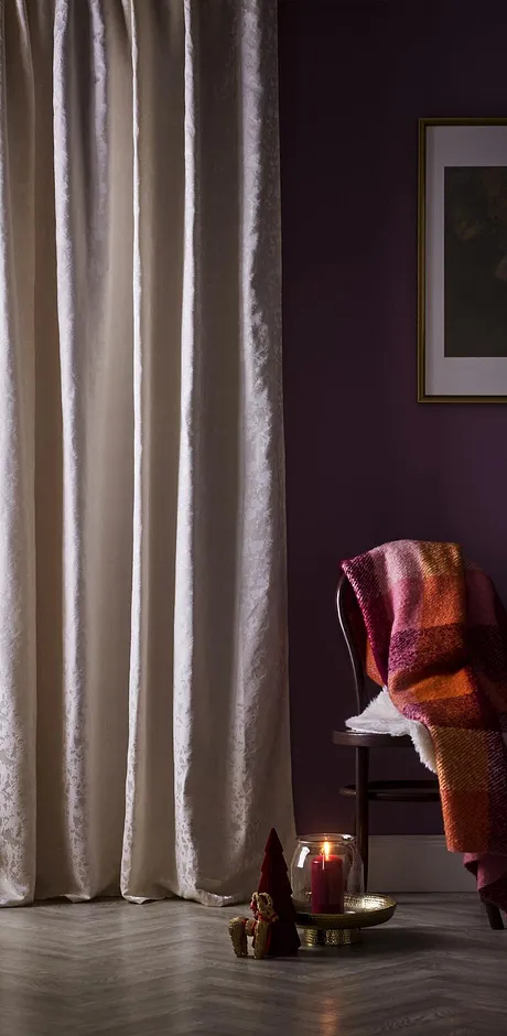 Ljusa gardiner pryder fönstret. En varm filt ligger över en stol.

